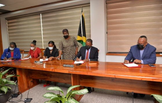 Minister of Finance and the Public Service Dr. Nigel Clarke (second right), and Minister of State Hon. Marsha Smith (center, seated), sign the Heads of Agreement formalizing the Government’s four per cent wage increase offer for April 2021 to March 2022 with executives of three of the six additional unions representing public sector workers that have accepted the provision.