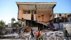 People walk past a home destroyed by the earthquake in Les Cayes, Haiti, Saturday, Aug. 14, 2021. A 7.2 magnitude earthquake struck Haiti on Saturday, with the epicenter about 125 kilometers (78 miles) west of the capital of Port- au-Prince, the US Geological Survey said. (AP Photo/Joseph Odelyn)