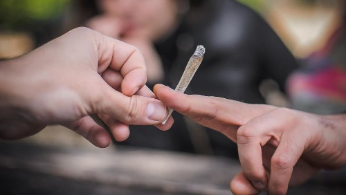 Closeup detail macro view of marijuana joint circling around from hand to hand. Young friends smoking cannabis marijuana ganja or hashish cigarette. Real life scene concept