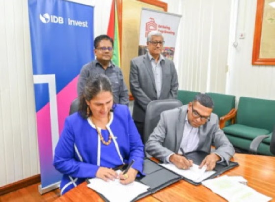 Finance Minister Dr. Dr Ashni Singh (left standing) looks on as the loan agreement is being signed between officials of IDB Invest and IPED.
