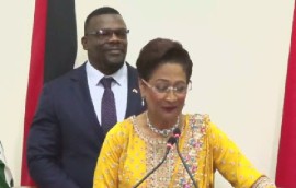 Prime Minister Kamla Persad Bissessar, speaking during Thursday night’s post cabinet news conference. Homeland Security Minister, Roger Alexander, stands behind her (CMC PHoto)