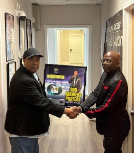 Singer Derrick Scott (right) accepts a plaque from broadcaster Clinton Lindsay, marking his song God Answers Prayers reaching number one on Lindsay's South Florida Reggae Chart 2021.